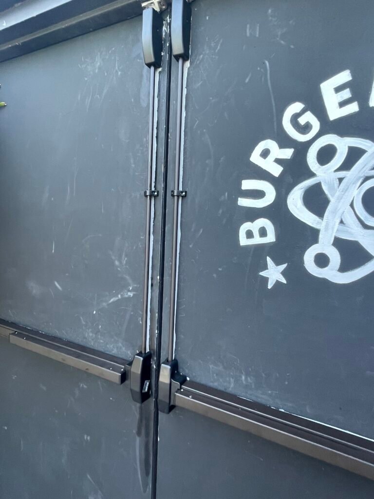 Surface-mounted vertical rod exit devices on the double doors at Burgerology in Patchogue