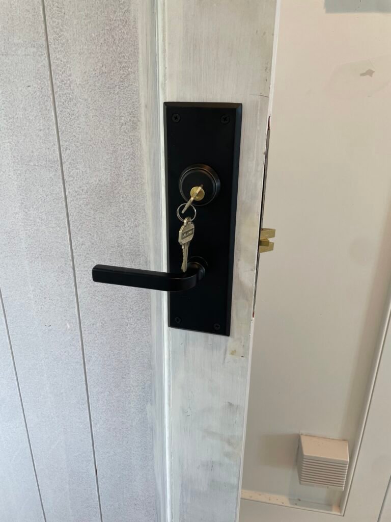 Original dark Baldwin mortise lock hardware retained during a cylinder replacement on Shore Road in East Setauket